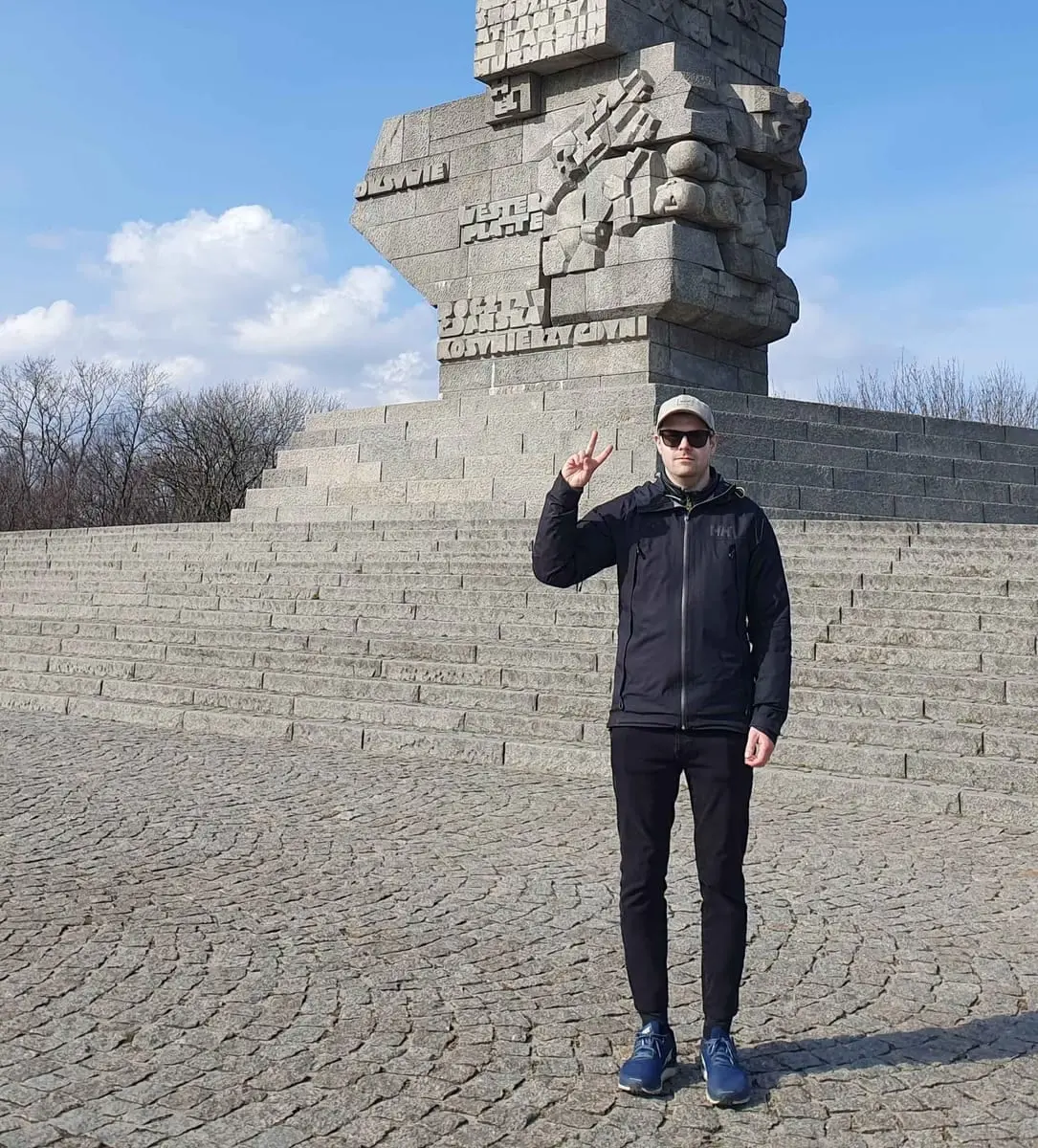 En mann med caps og solbriller gjør fredstegn foran Westerplatte-monumentet