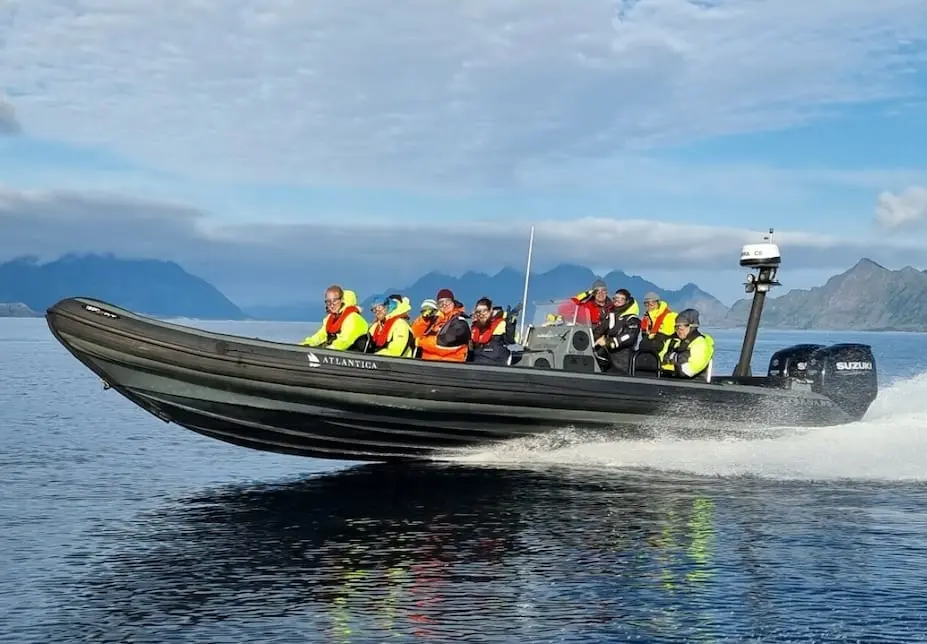 Kolleger i redningsdrakter på RIB-tur i høy fart over sjøen, med fjell i bakgrunnen