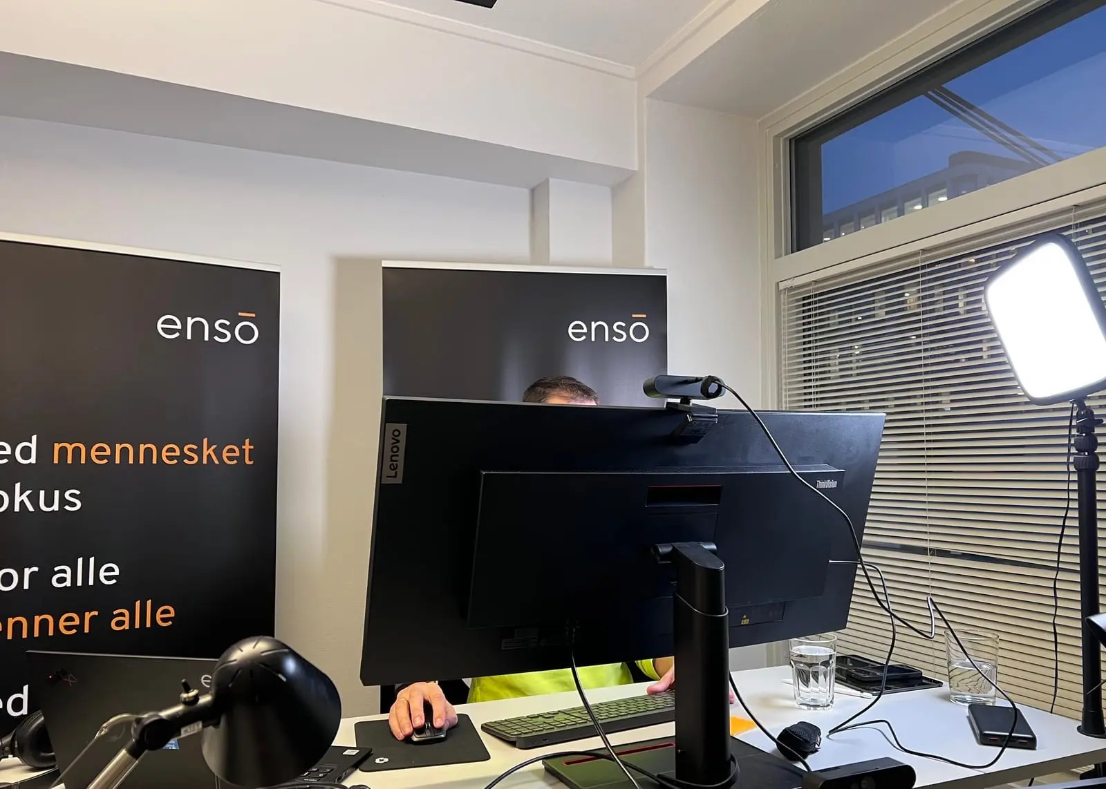 En person bak en skjerm med webkamera og videolys foran Ensō-roll-ups under workshopen
