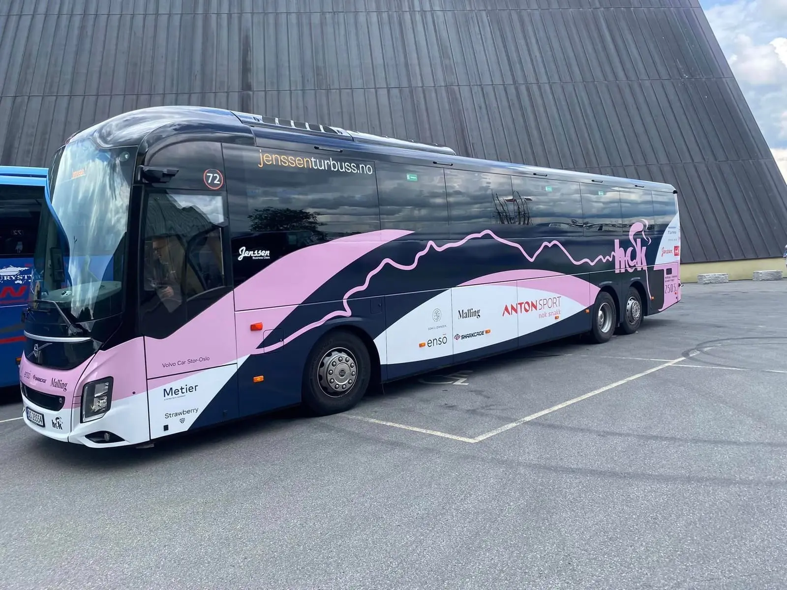 Klubbens turbuss i rosa og mørkeblått med sponsorlogoer, blant annet Ensō