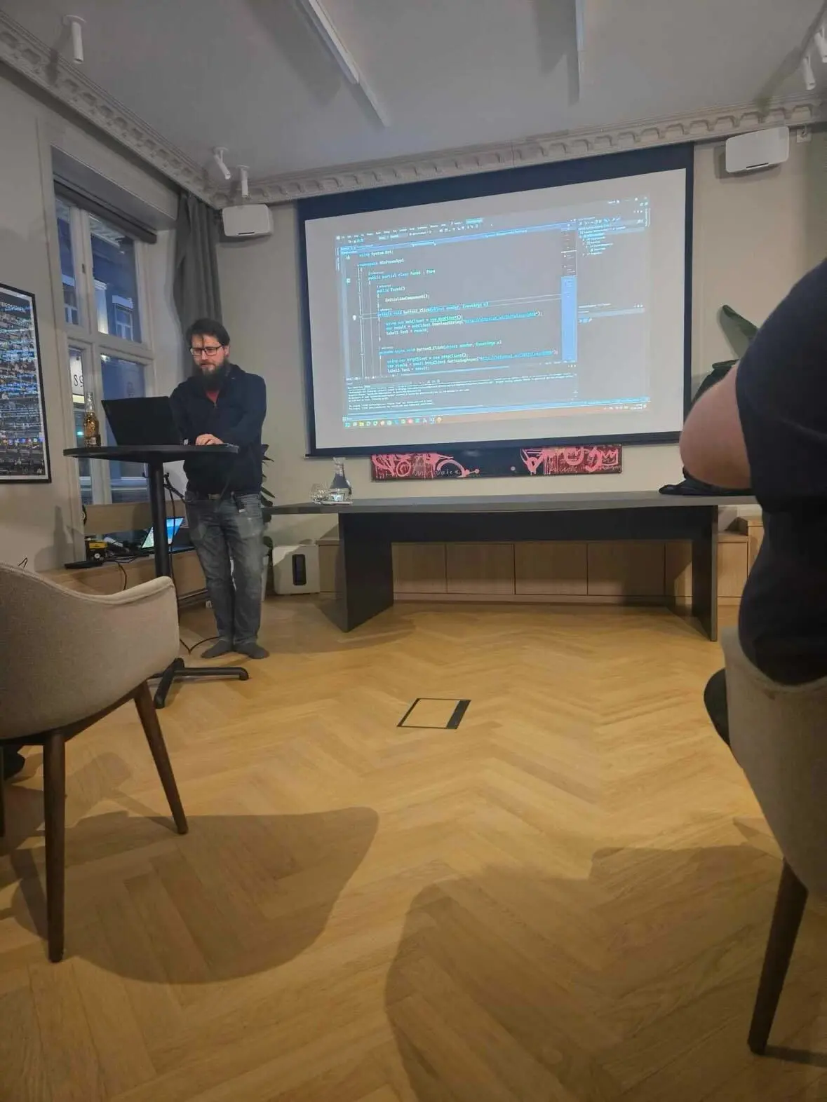 Oddbjørn står ved en ståpult og viser C#-kode med async og await på lerretet