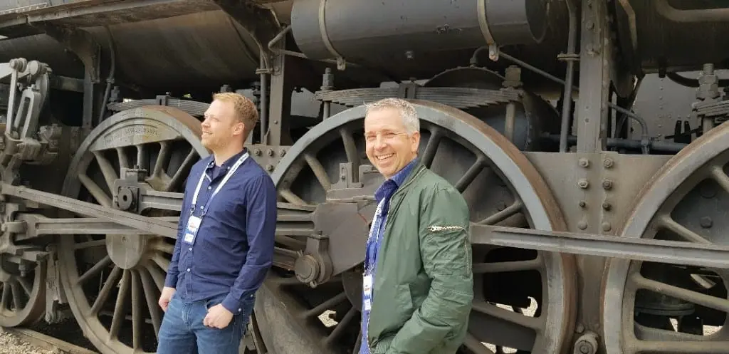 Torstein og Snorre med konferansebånd foran de store hjulene på et gammelt damplokomotiv