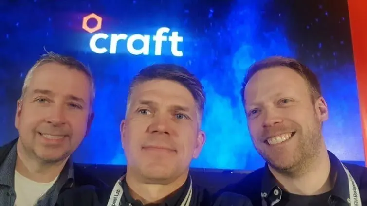 Tre smilende menn tar selfie foran en stor skjerm med Craft-logoen