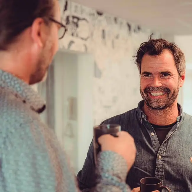 To kolleger med kaffekopper ler sammen på kontoret.