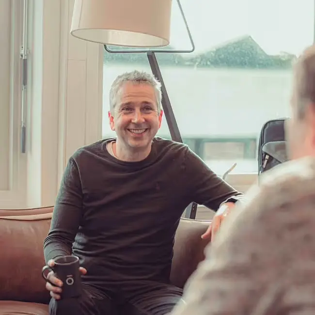 En kollega smiler med kaffekoppen i hånden i sofaen på kontoret.